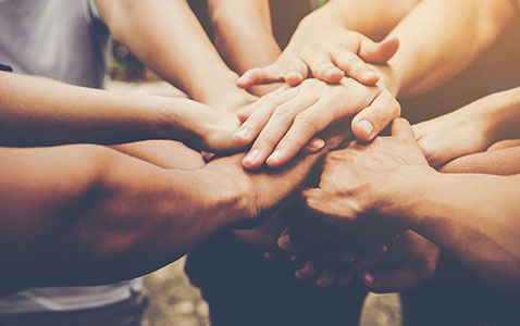 Menschengruppe reicht Hände zueinander, Symbol für Kooperation und Gemeinschaft, Quellenangabe: RANA – stock.adobe.com